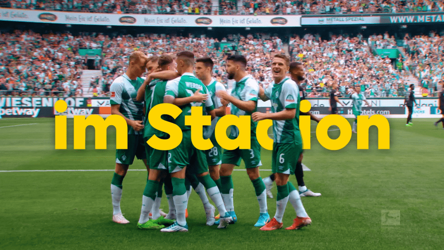 Jubelndes Fußballteam im Stadion mit integrierter gelber Typografie.